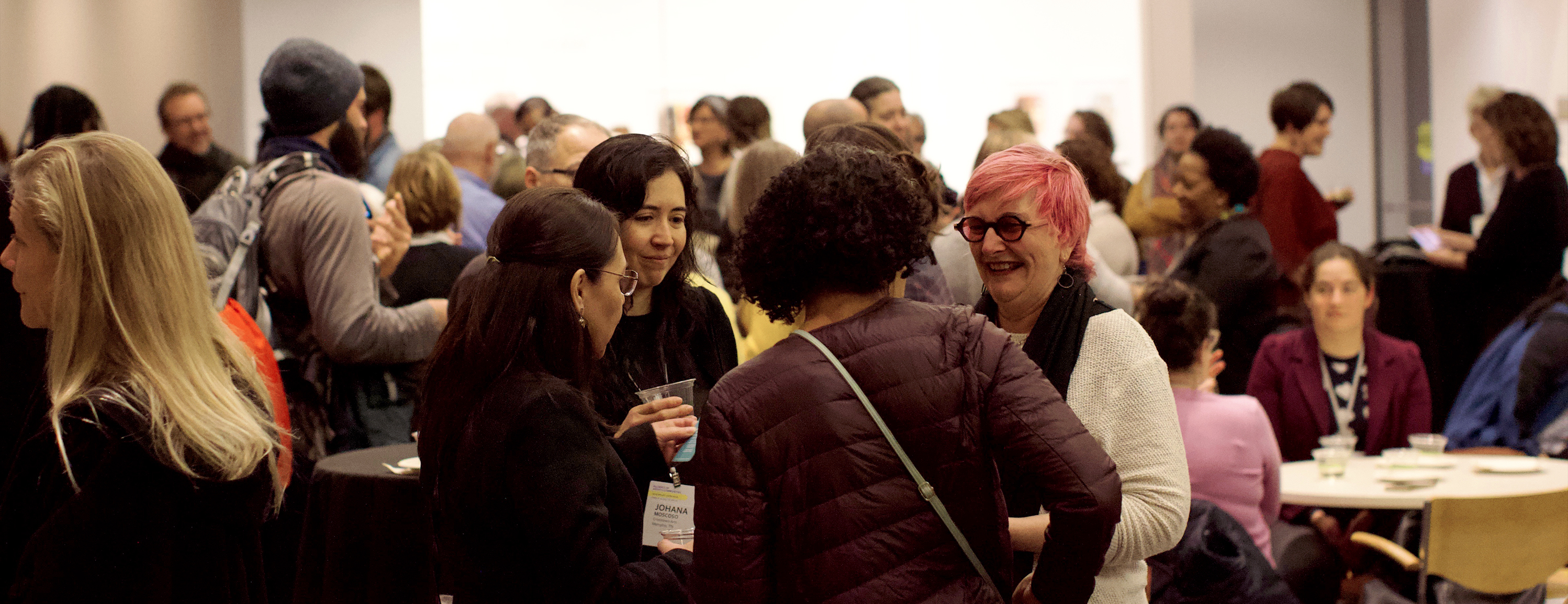 A group of four people talking in a circle surrounded by many other people in a conference room.