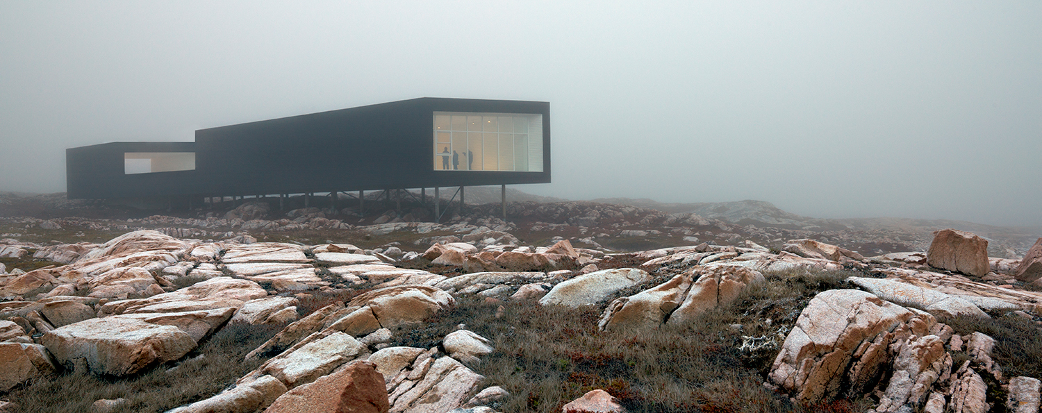 A building on stilts in a foggy setting above rocky terrain. 