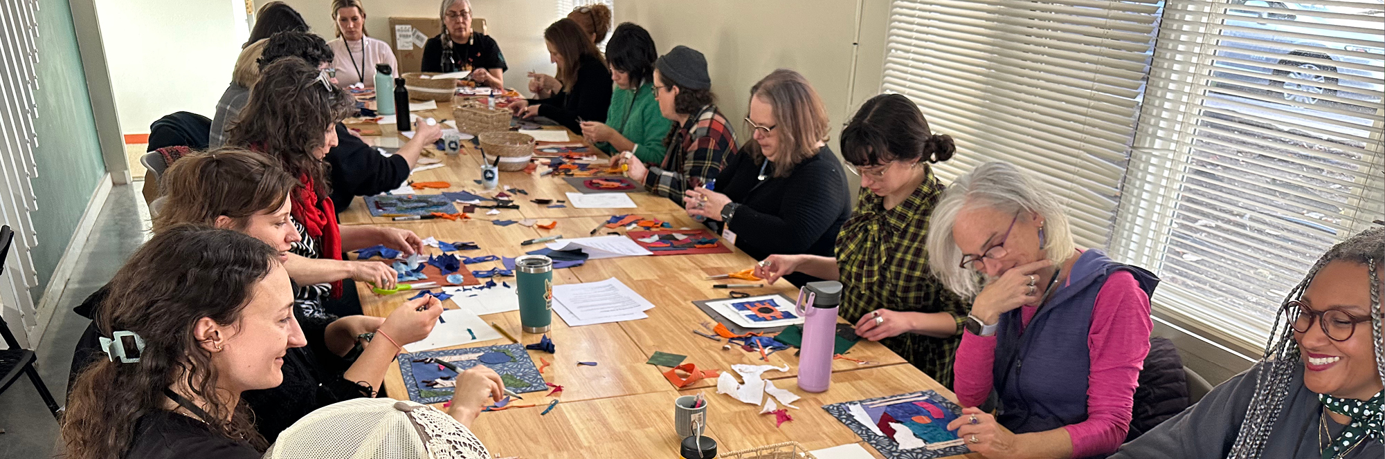 A group of people sitting around a table creating using scraps of colorful fabric.