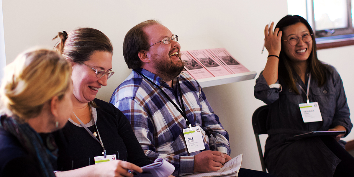 Four people wearing conference badges laugh and take notes