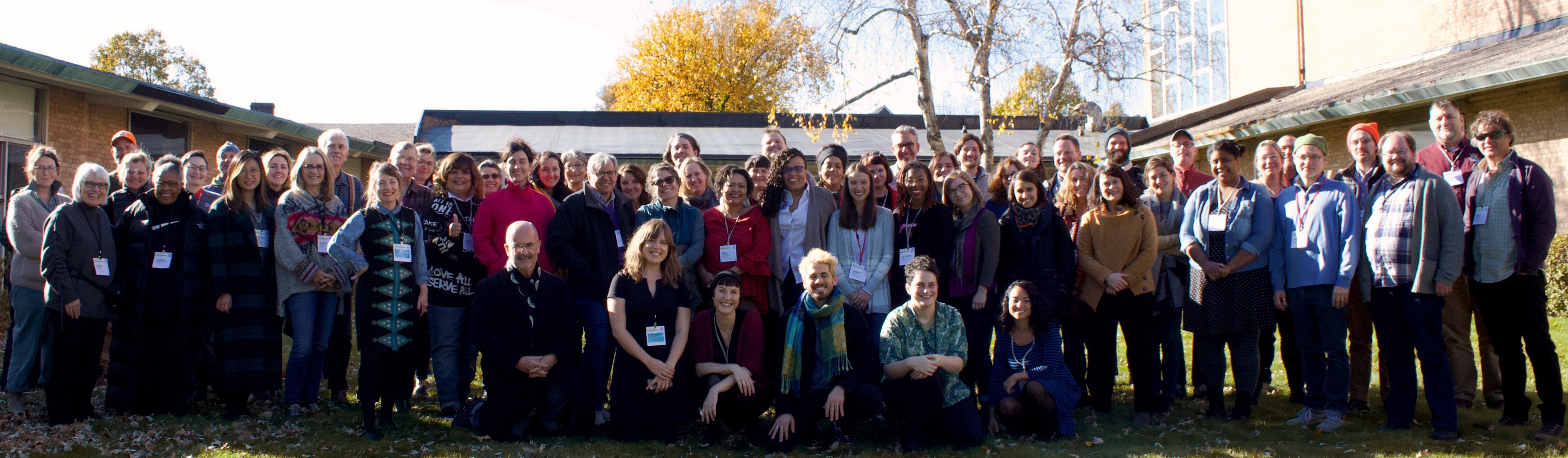 a large group of smiling people gather on the grass in front of a white building for a group photo