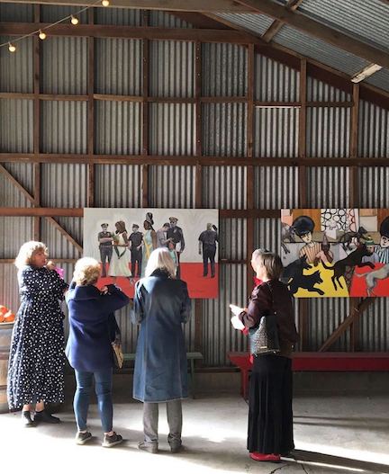 A group of five people looking at two paintings with their back turned to the camera.