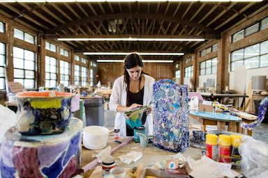 A person in a studio space surrounded by sculptural items.