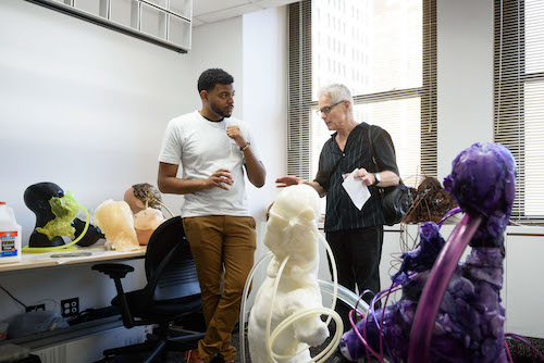 Image Description: Artist Terrance James Jr. talking to a visitor in his studio about his sculptural work in the foreground.
