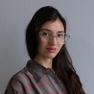 A photo of Ellena Basada - a woman with long dark hair and glasses in a grey button up shirt