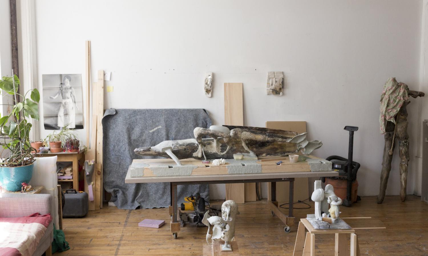Various artworks, materials, and a table against a white wall. Photographer: Brad Ogbonna