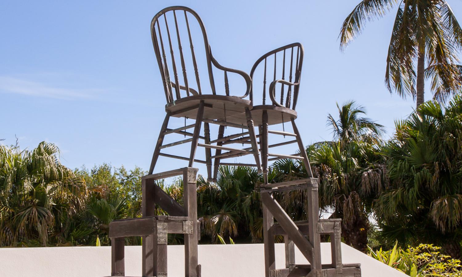 An outdoor sculpture of two chairs facing one another and sitting on a ladder like structure