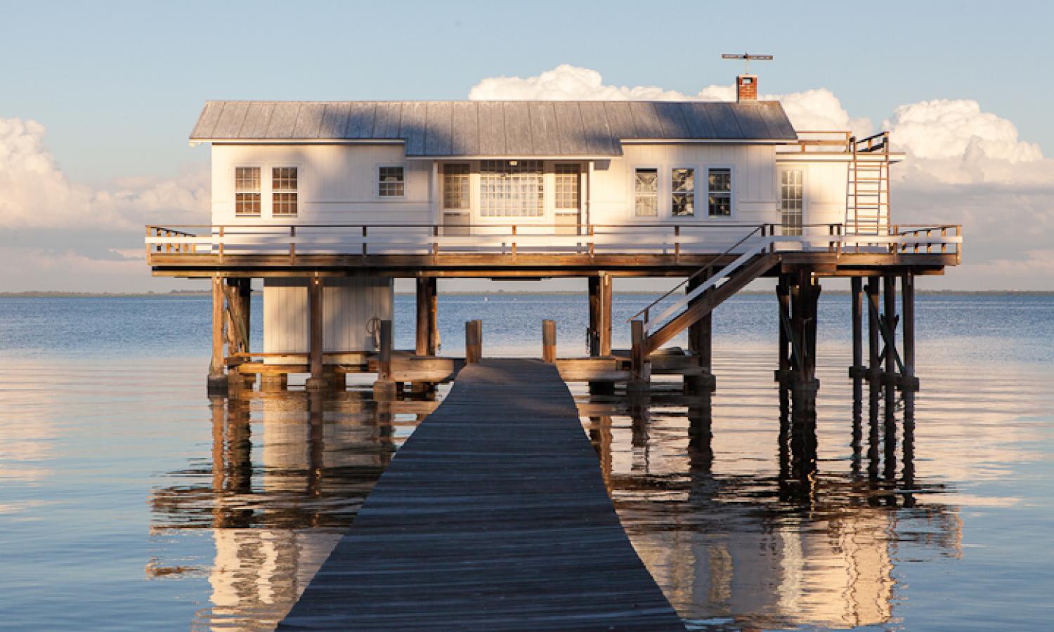 A white house on stilts with a wooden deck leading to it