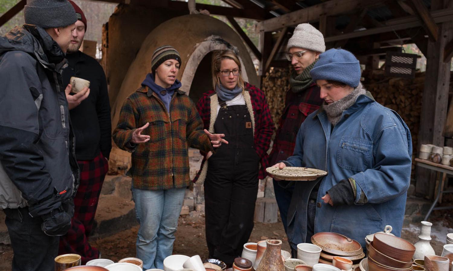 potters gathered outside a wood kiln after unloading, discussing the pottery
