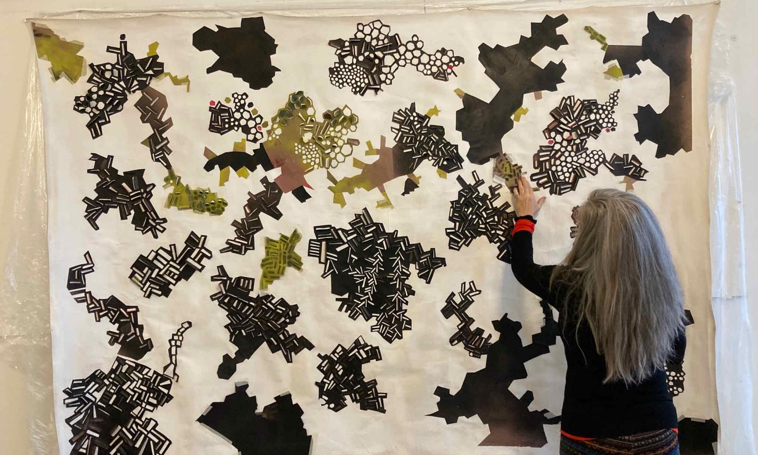 Carrie Dickason arranges elements of black and white patterned shapes on a large canvas at StudioWorks.