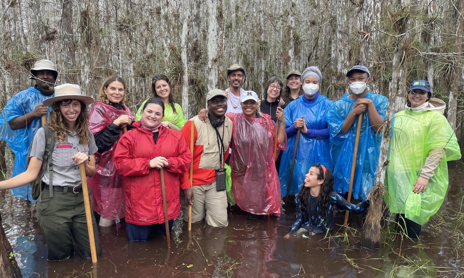 AIRIE Fellows and Friends on a Slough Slog. Knee deep in water, surrounded by Cypress trees, wearing colorful ponchos, and smiles.