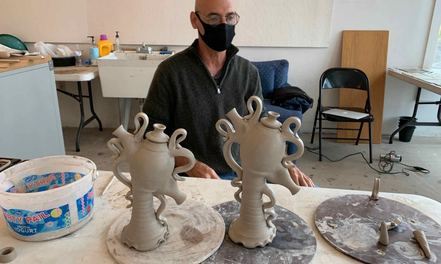 Herb Weaver sits behind ceramic teapot sculptures artwork in the studio. As part of his residency, Weaver worked with students at local schools and hosted community members to work on a collaborative piece.
