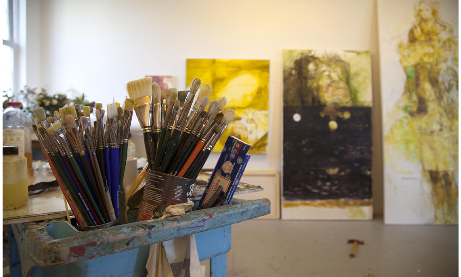 Brushes in an artist's studio with paintings in the background