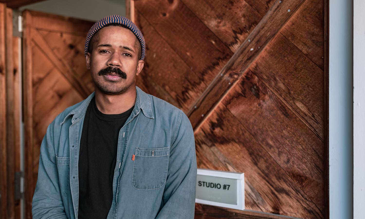 Visual Arts Fellow, Kevin Brisco, standing in front of their studio door (Photo Credit: Michael Cestaro)