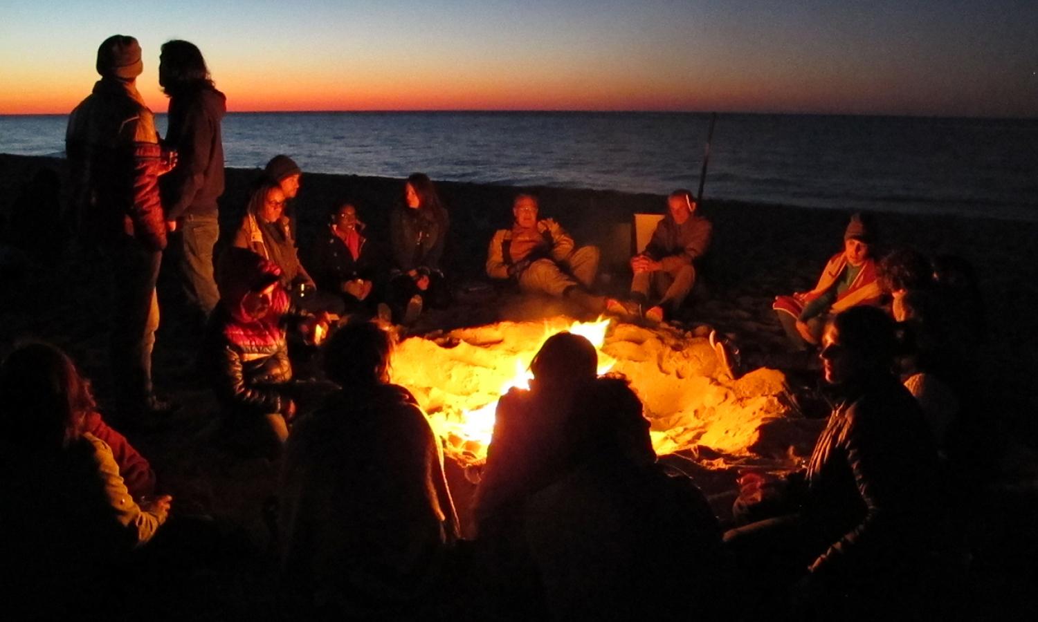 Fellows seated around a beach bonfire