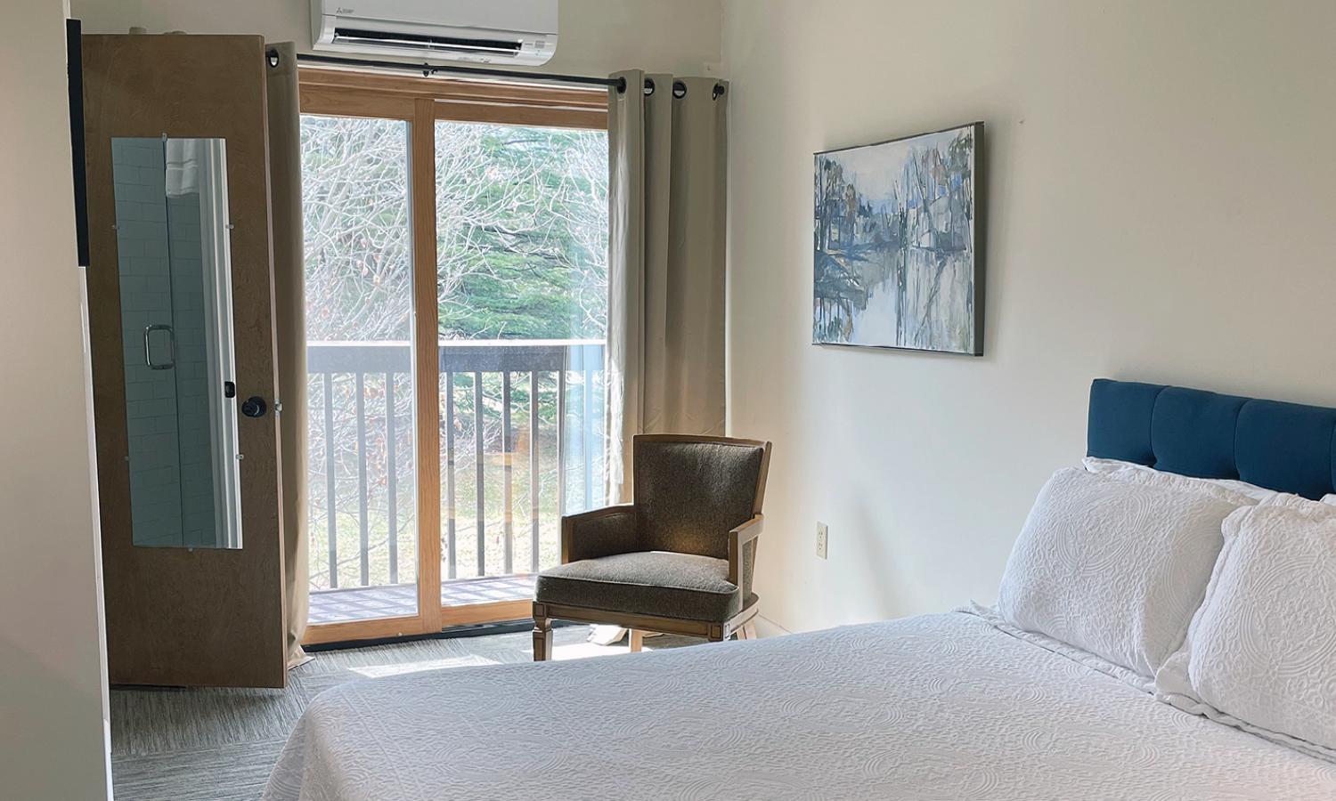 Bedroom with double bed, reading chair, sliding glass doors, and private bathroom.