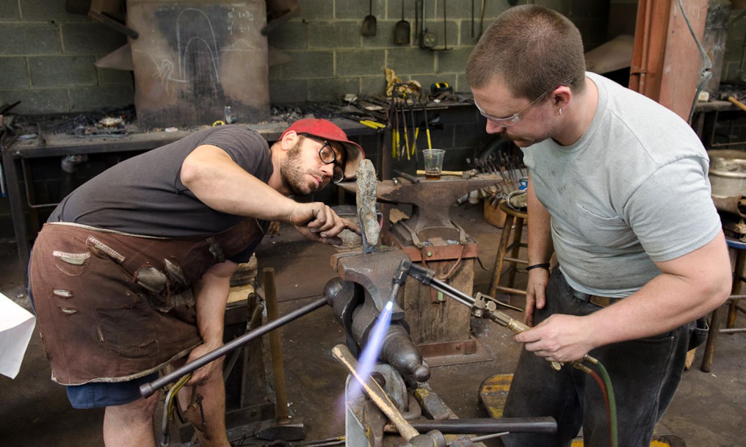 Core fellows Daniel Beck and Seth Gould working together in a blacksmithing workshop