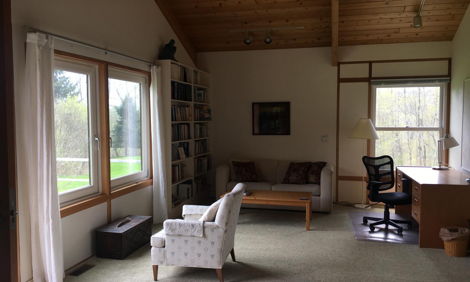 a carpeted room with vaulted ceiling, large writing desk, and chair positioned in front of two large windows