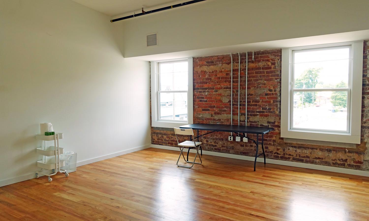 Hardwood floors, white walls, and sun pouring in through the windows of the studio space