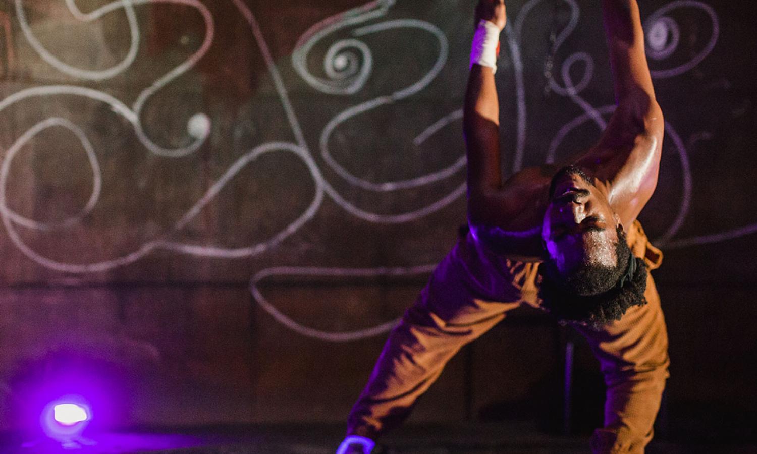 Dancer in partial backbend in brown pants with abstract drawing in background