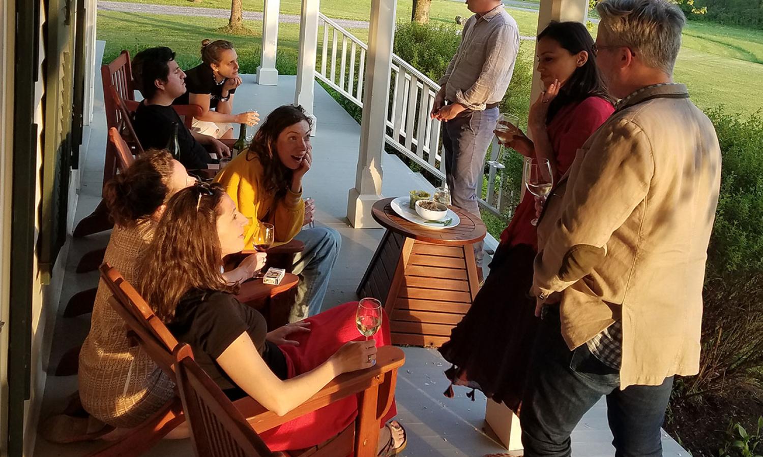 Various residents gathered on porch of house with wine and snacks