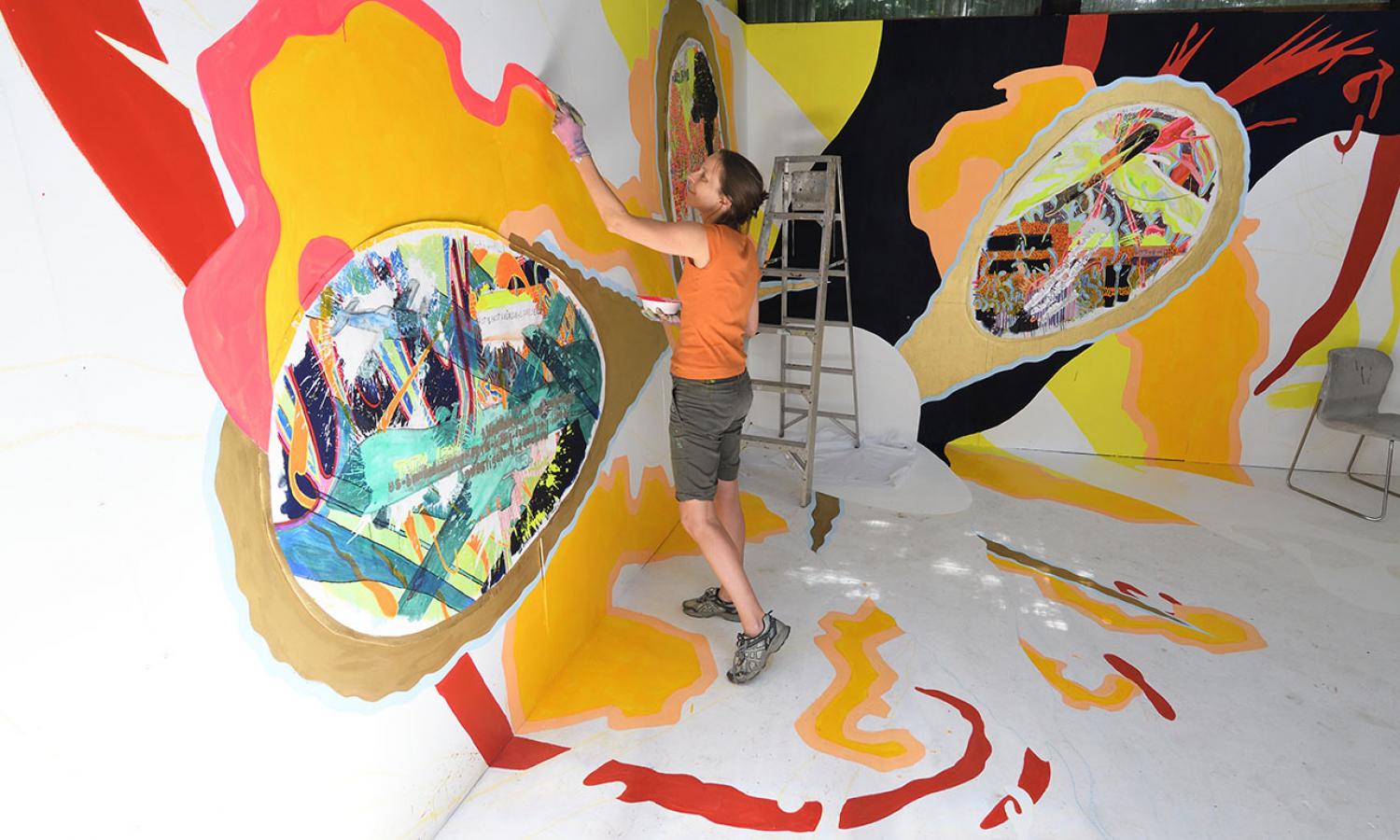 Resident in orange shirt painting a large mural