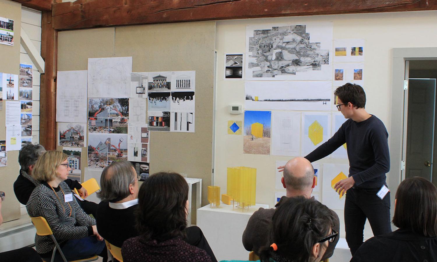 Architecture resident presenting small models and other images to a seated audience