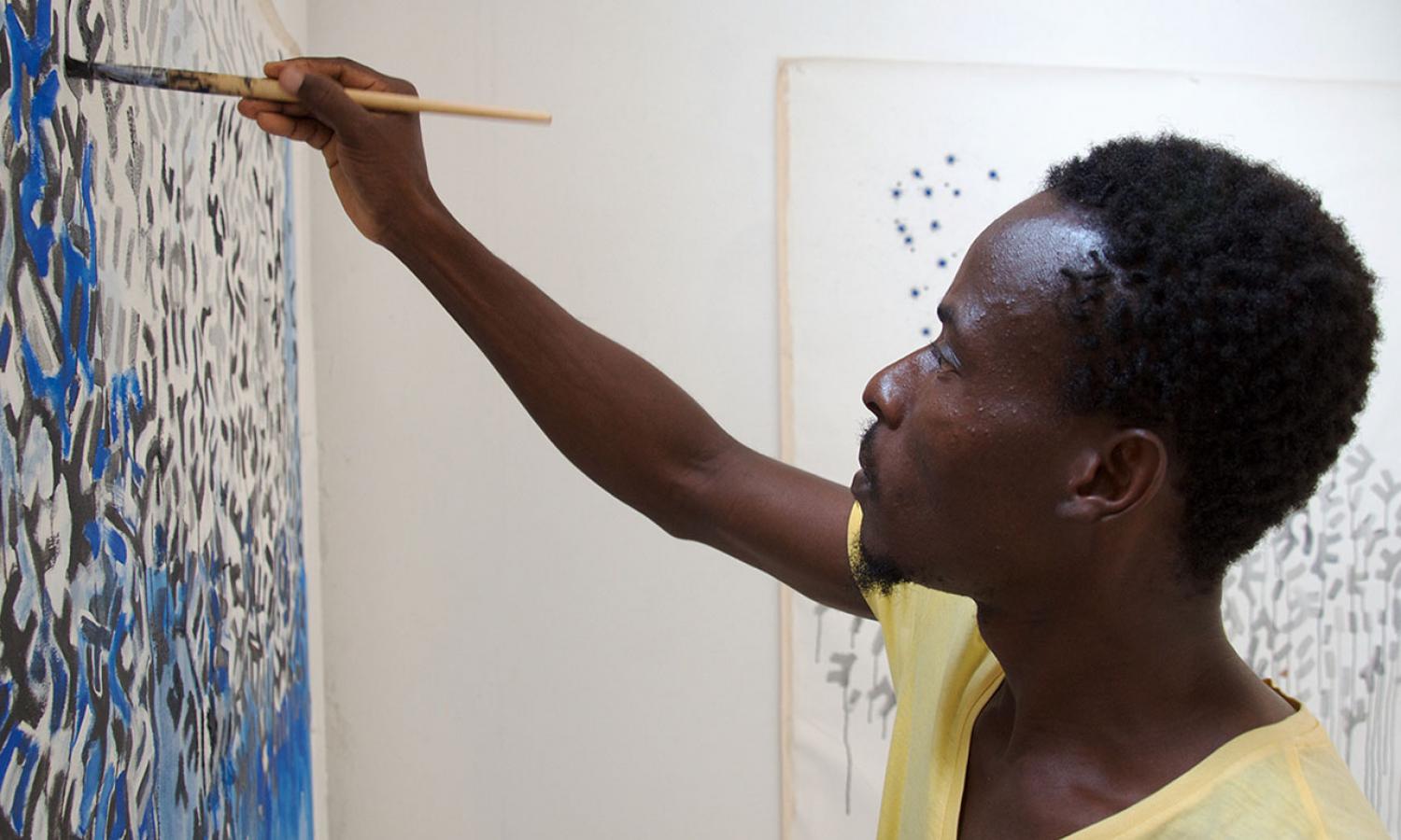 Artist in yellow shirt working on painted piece composed of abstract lines