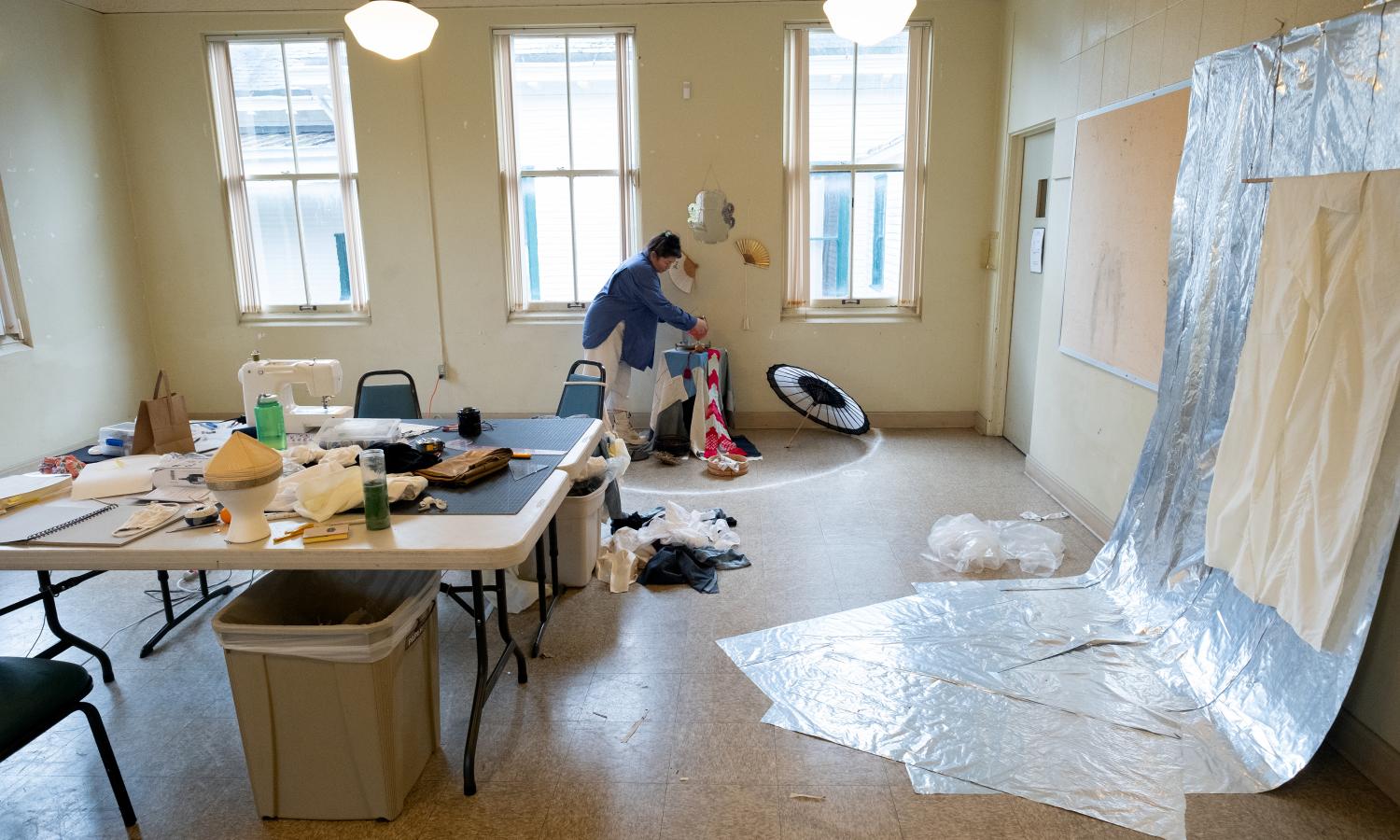 Image of Mel Carter working in large studio with tables and various materials around the room.