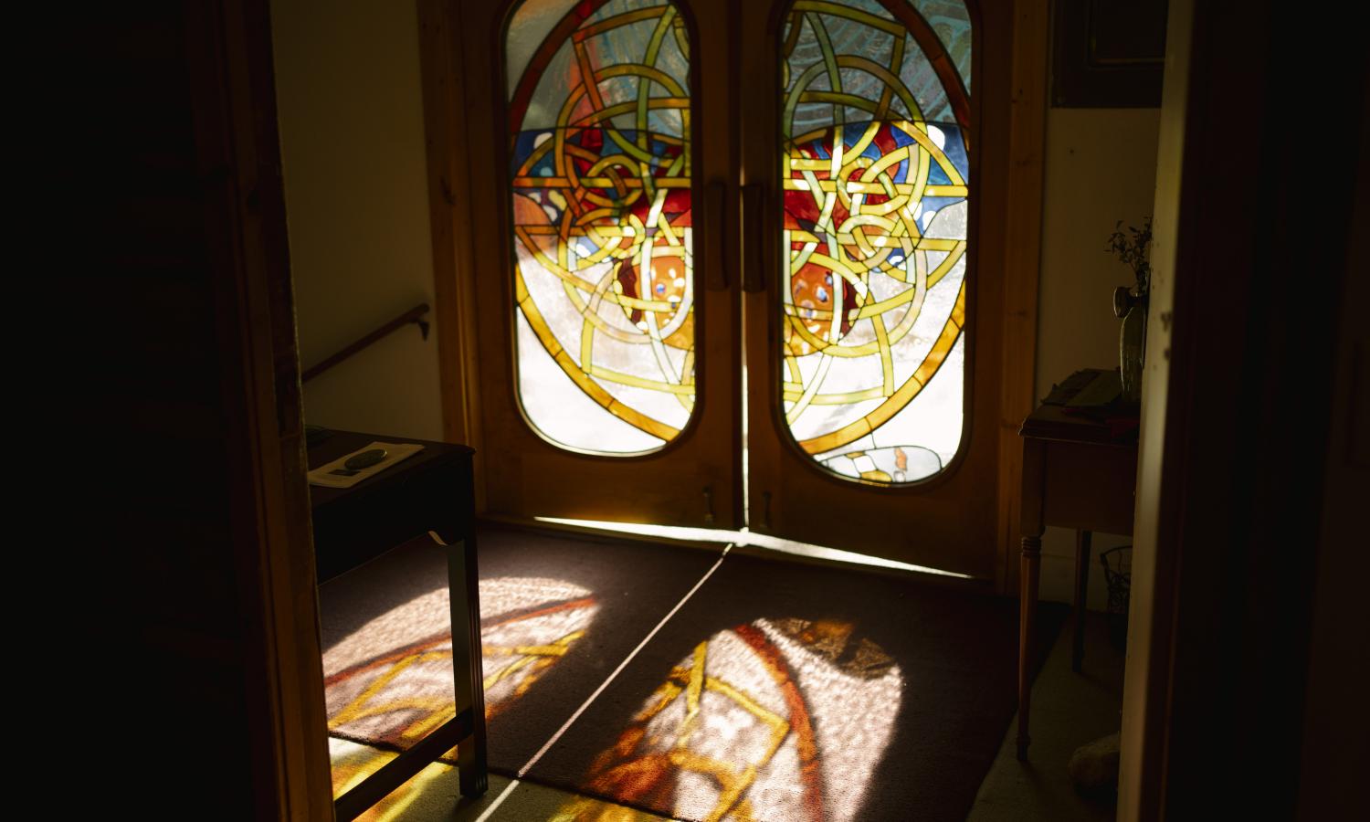 A stained glass double door entrance to the Grunewald Guild with light casting through its panes, illuminating a number of colors in the shape of a butterfly.