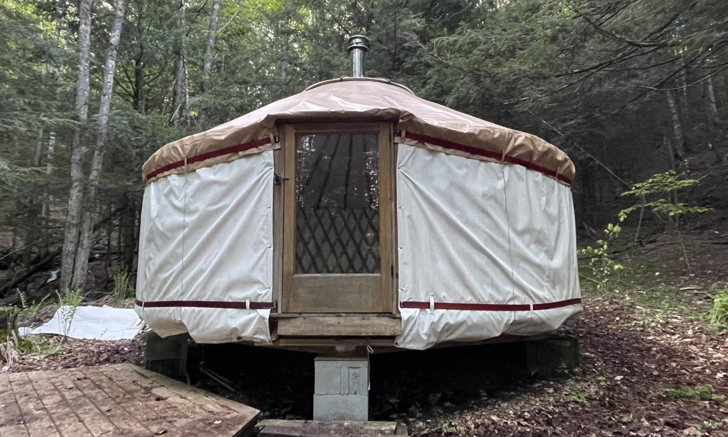 Large off-white yurt with a tan roof in the woods