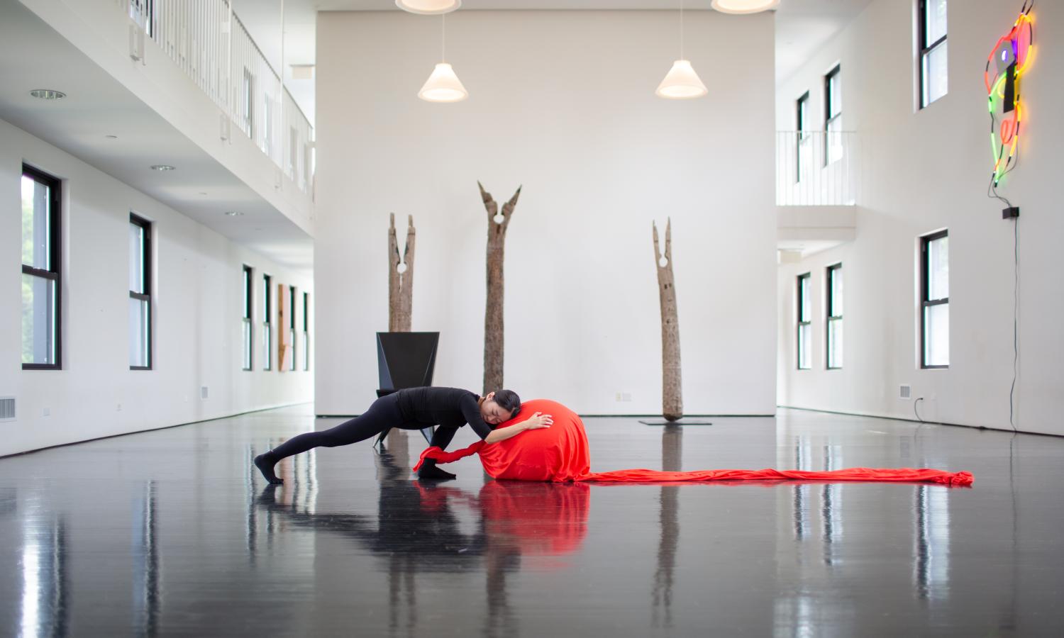 A performer clad in all black leans against a large ball that is wrapped in red fabric.