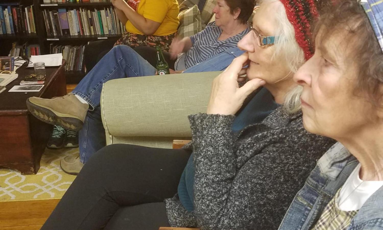 Community members sit in a row listening to the residents' share night, with one holding her hand over her mouth in concentration.