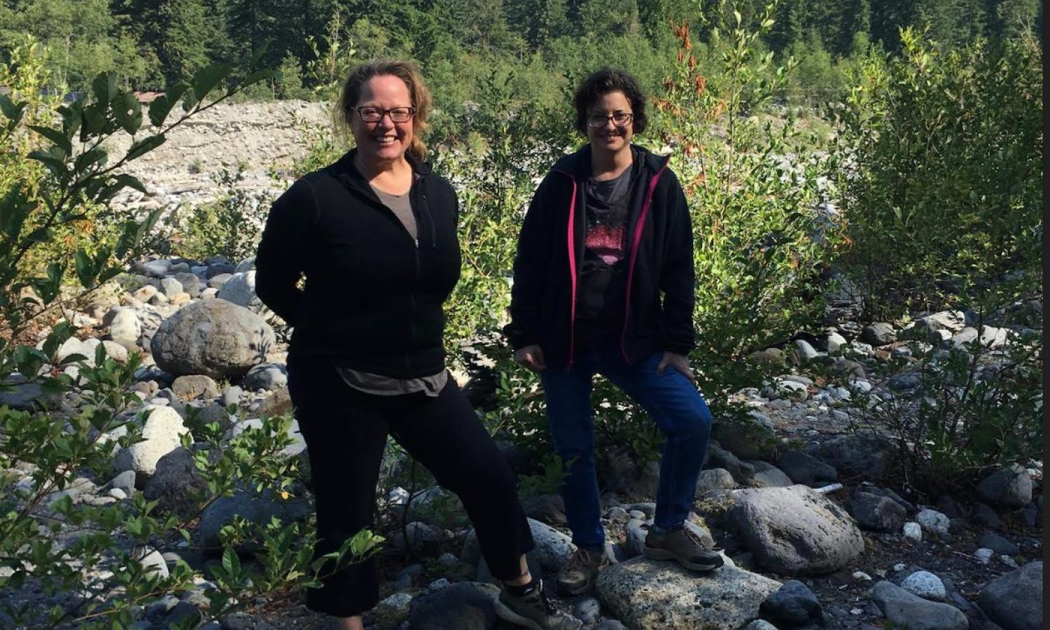 Two artists outside on a hike, posed in front of a meadow with Mt. Rainier in the background.