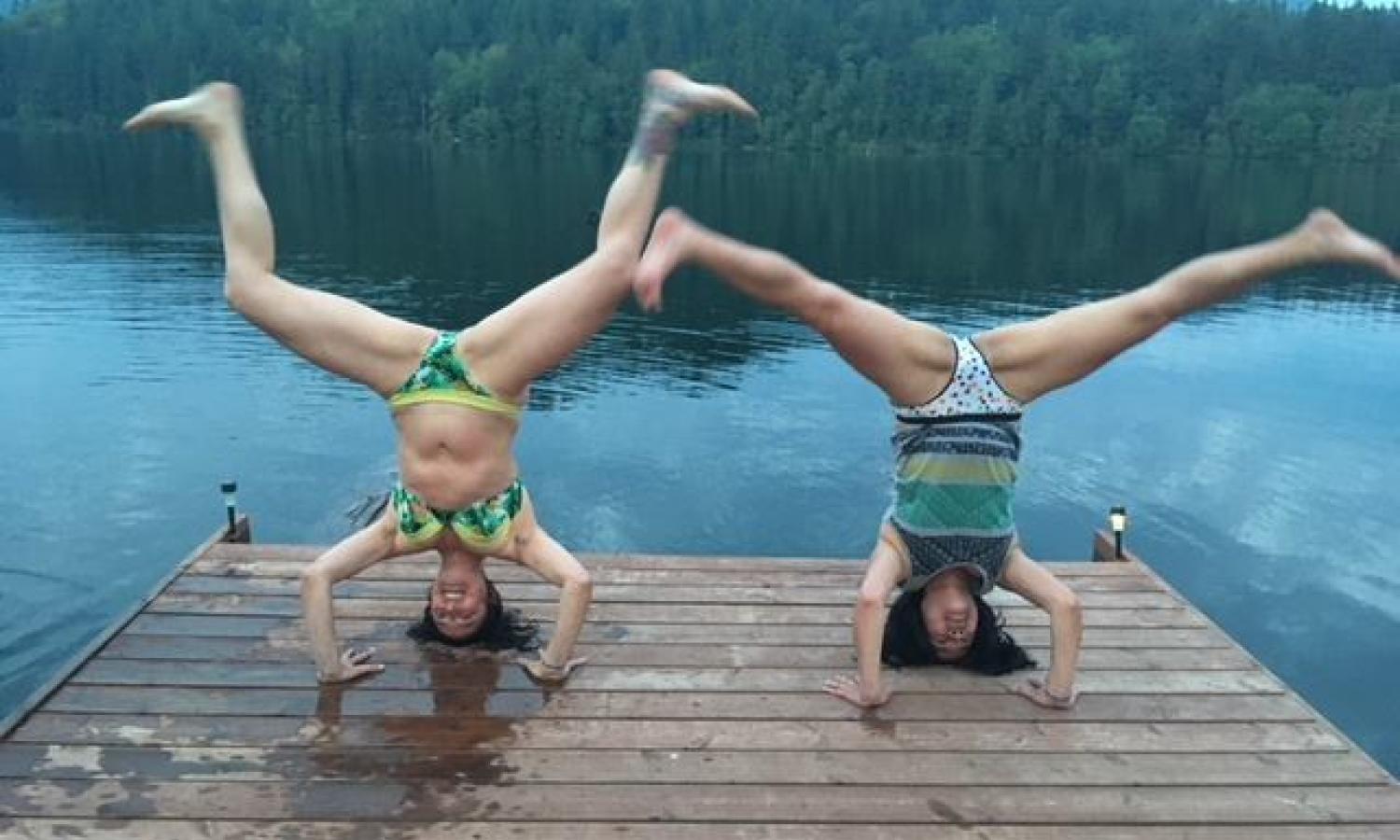 Two women in bikinis do headstands on a dock lining Mineral Lake.