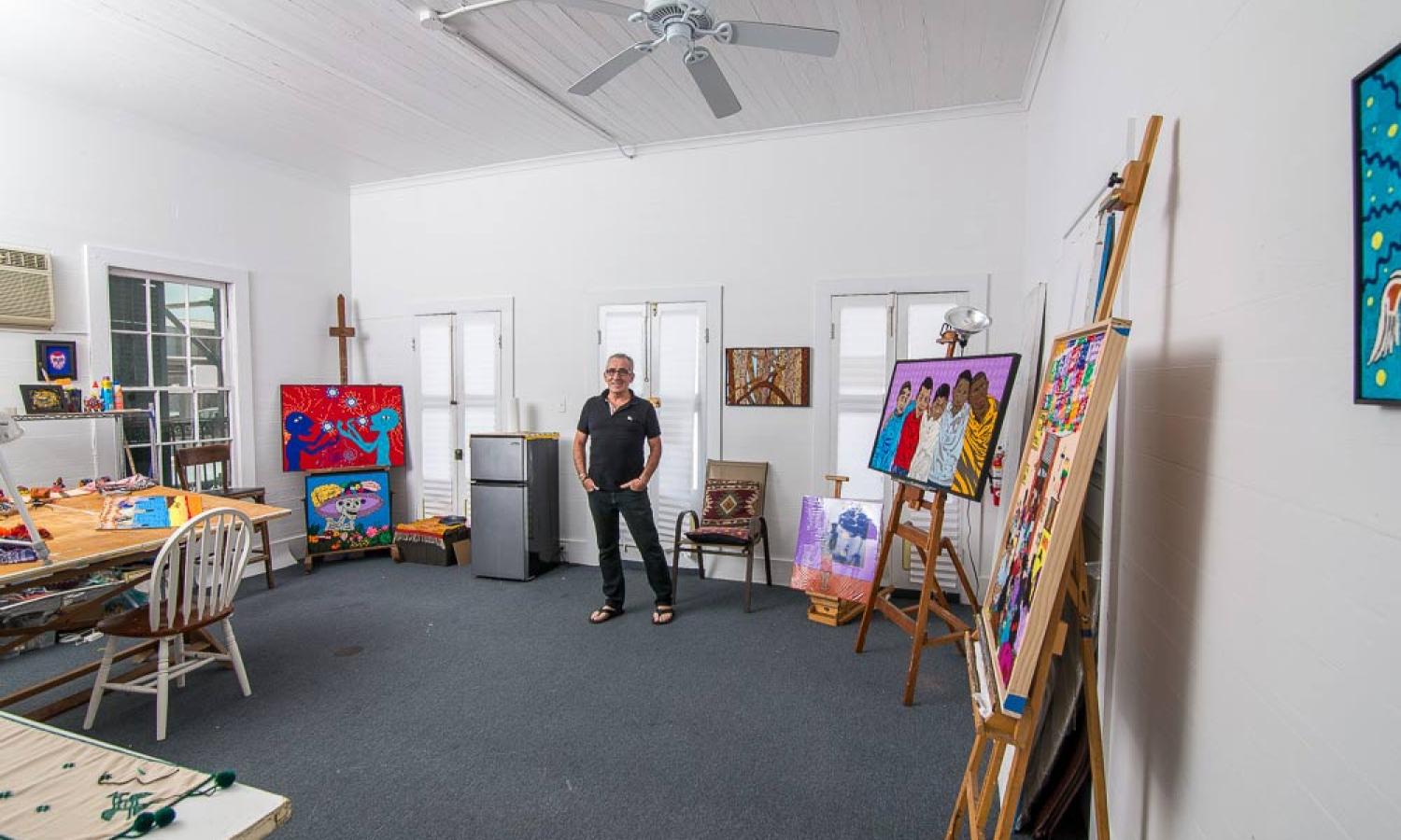 Male fiber artist and painter stands in the middle of a bright residence space with several colorful works on easels.