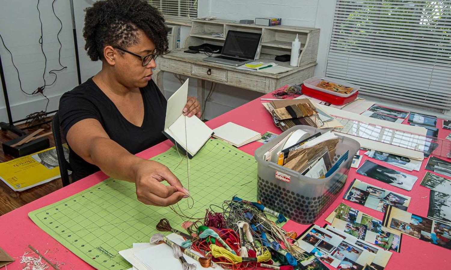 BIPOC female bookmaker attaches paper to a cover with thread.