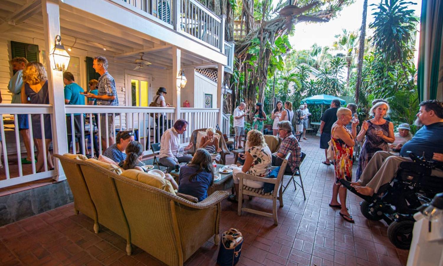 Outdoor gathering of several people in the Residency Courtyard with two levels of porch balconies and a large Banyan tree in the distance.