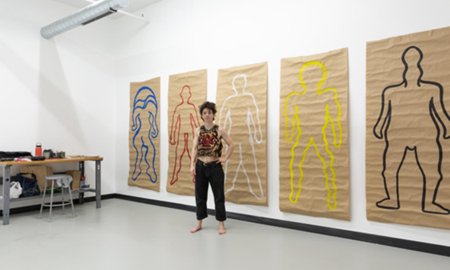 Residnt Lyra Hil in Studio with their work on the walls (2023)