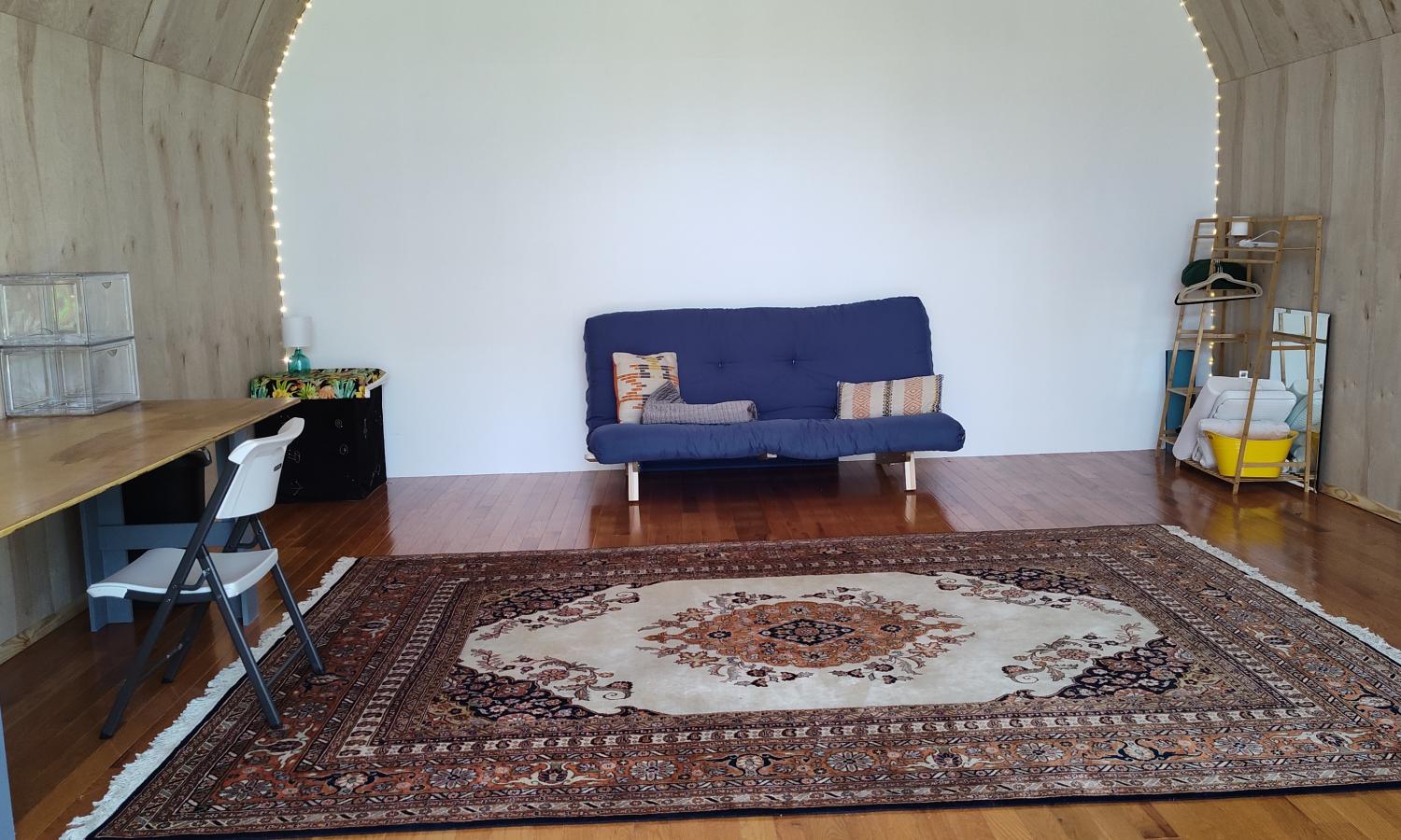 View of half the studio space which includes a large worktable on the left, a convertable futon sofa against the back wall, and mirrors on the right.  The space has a rounded ceiling