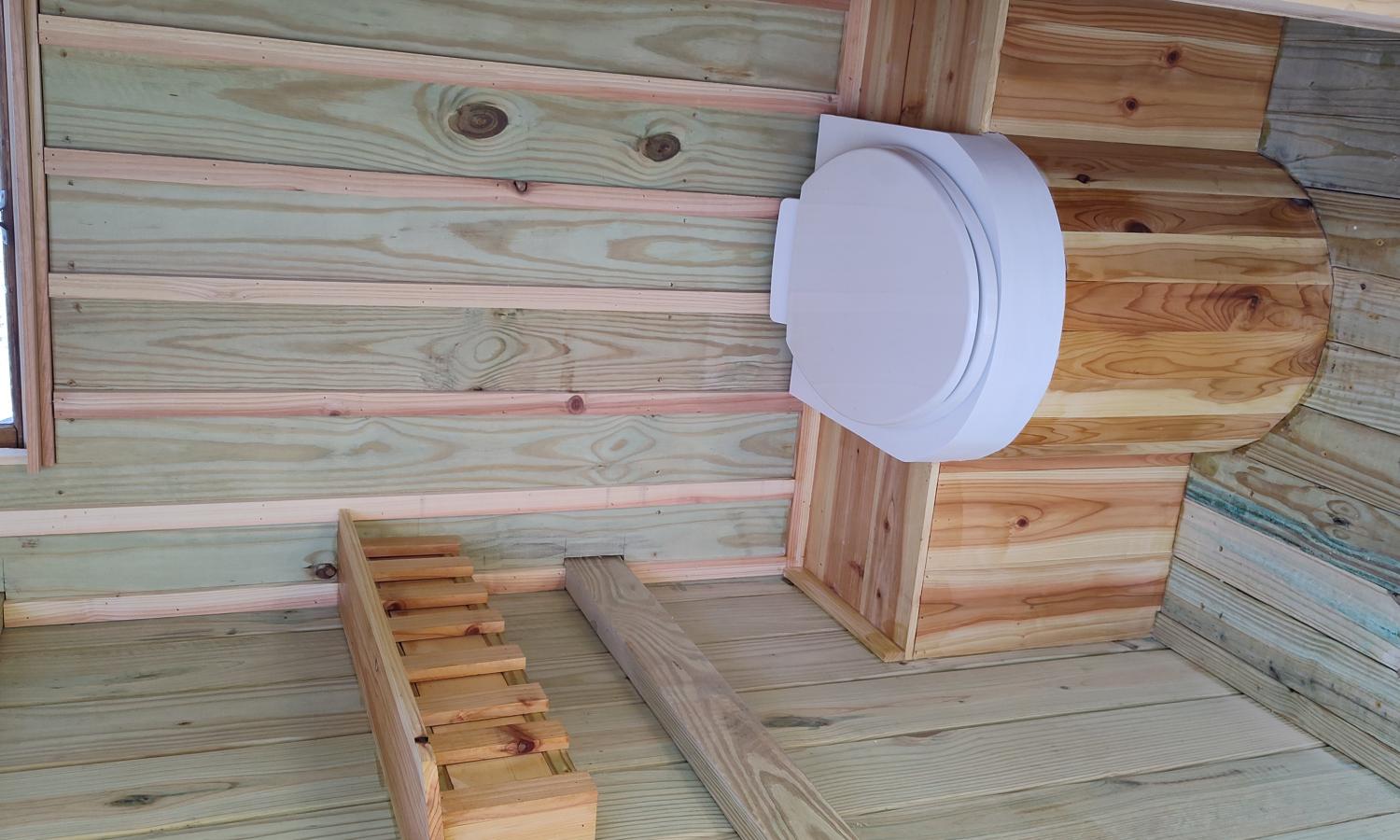 View from the outside porch into a bathroom stall including the seat of a composting toilet