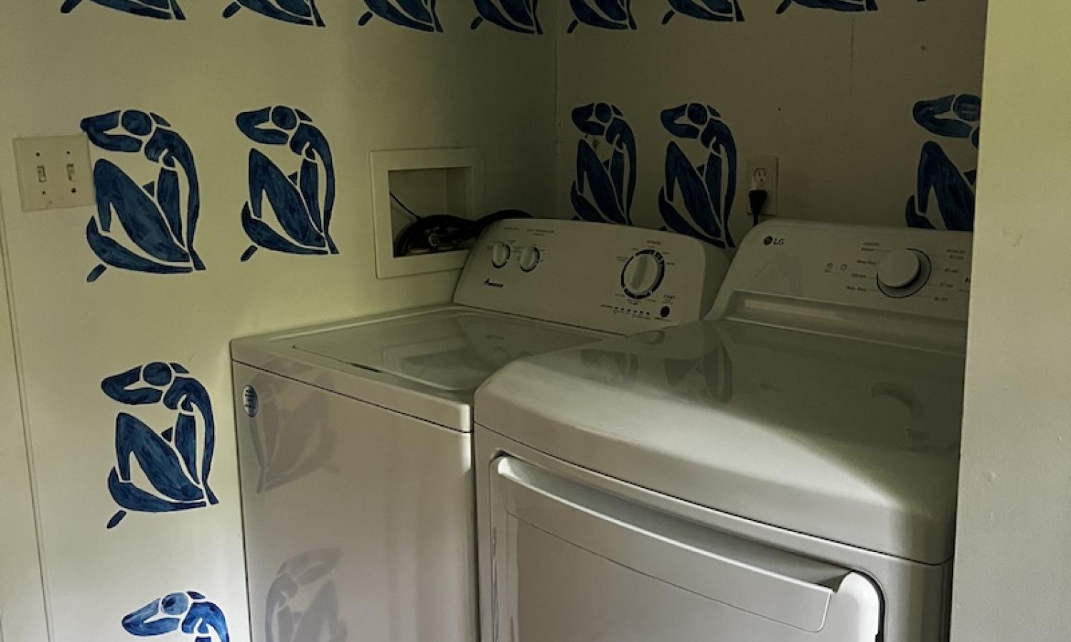 A white washer and dryer tucked into a nook with white walls, painted with blue women