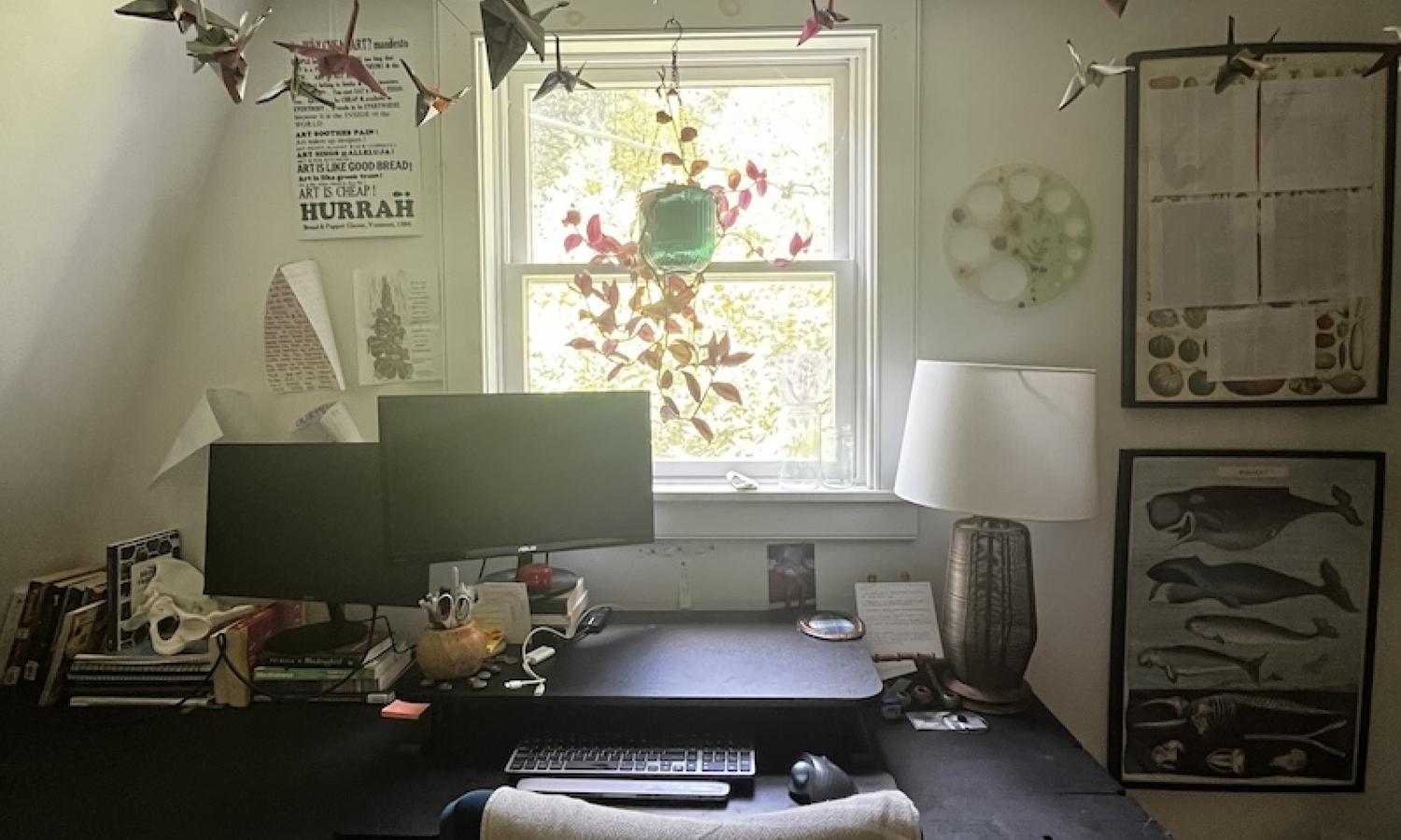 An office with a large desk, two monitors, and paper cranes hanging from the ceiling