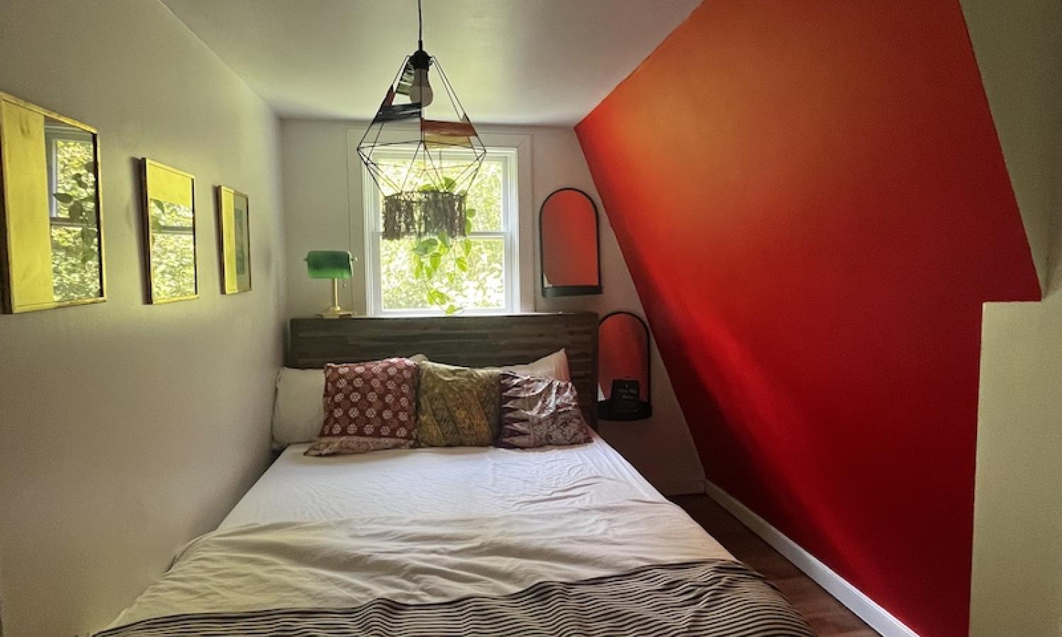 A small bedroom with white walls and one red,  slanted wall