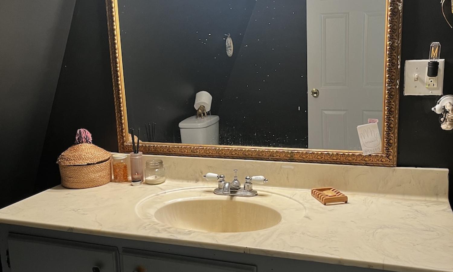 a bathroom vanity with a sink, large mirror against a black wall.