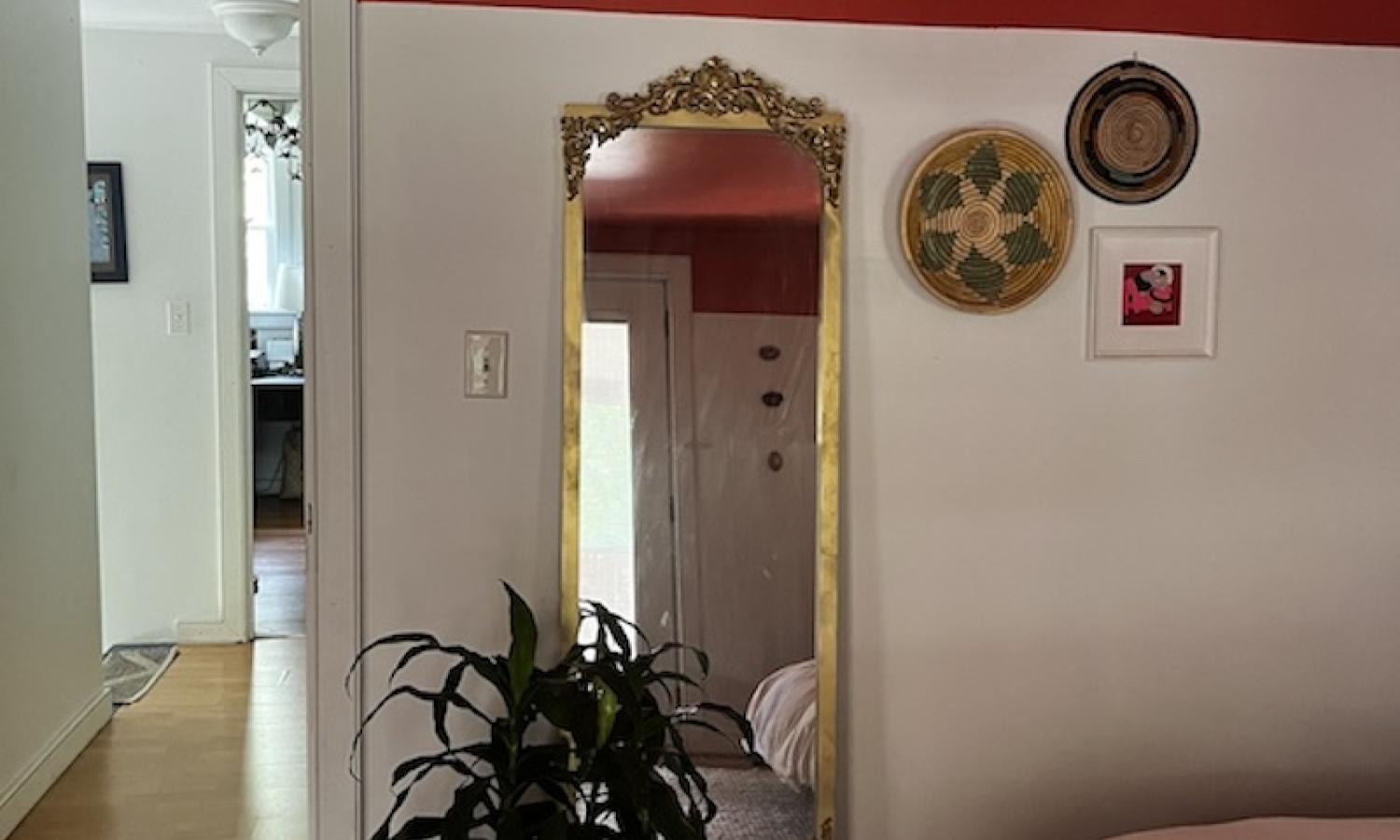 Golden, full length mirror with a plant and corner of a bed