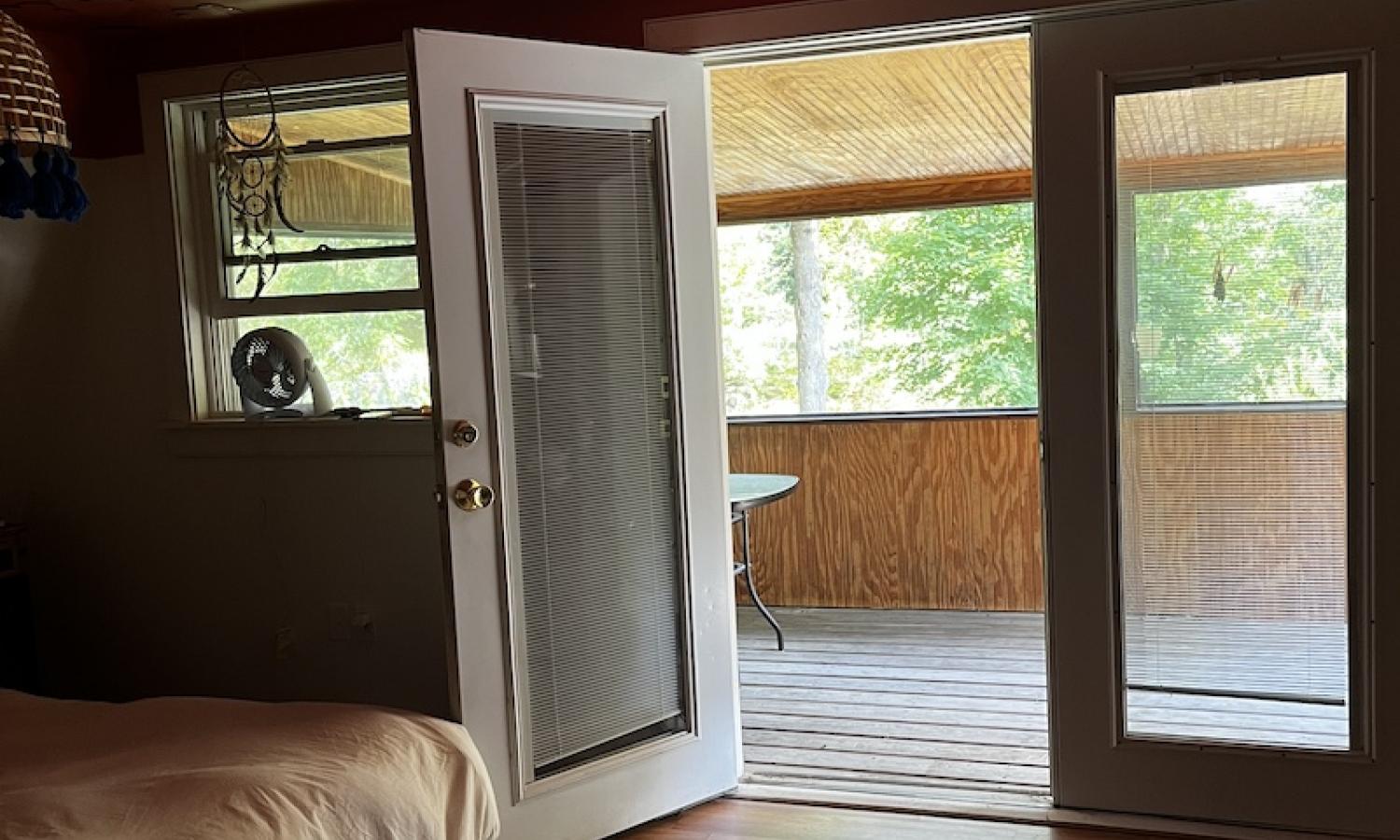 A door is open to a deck in a room with a large, white bed and coral ceiling