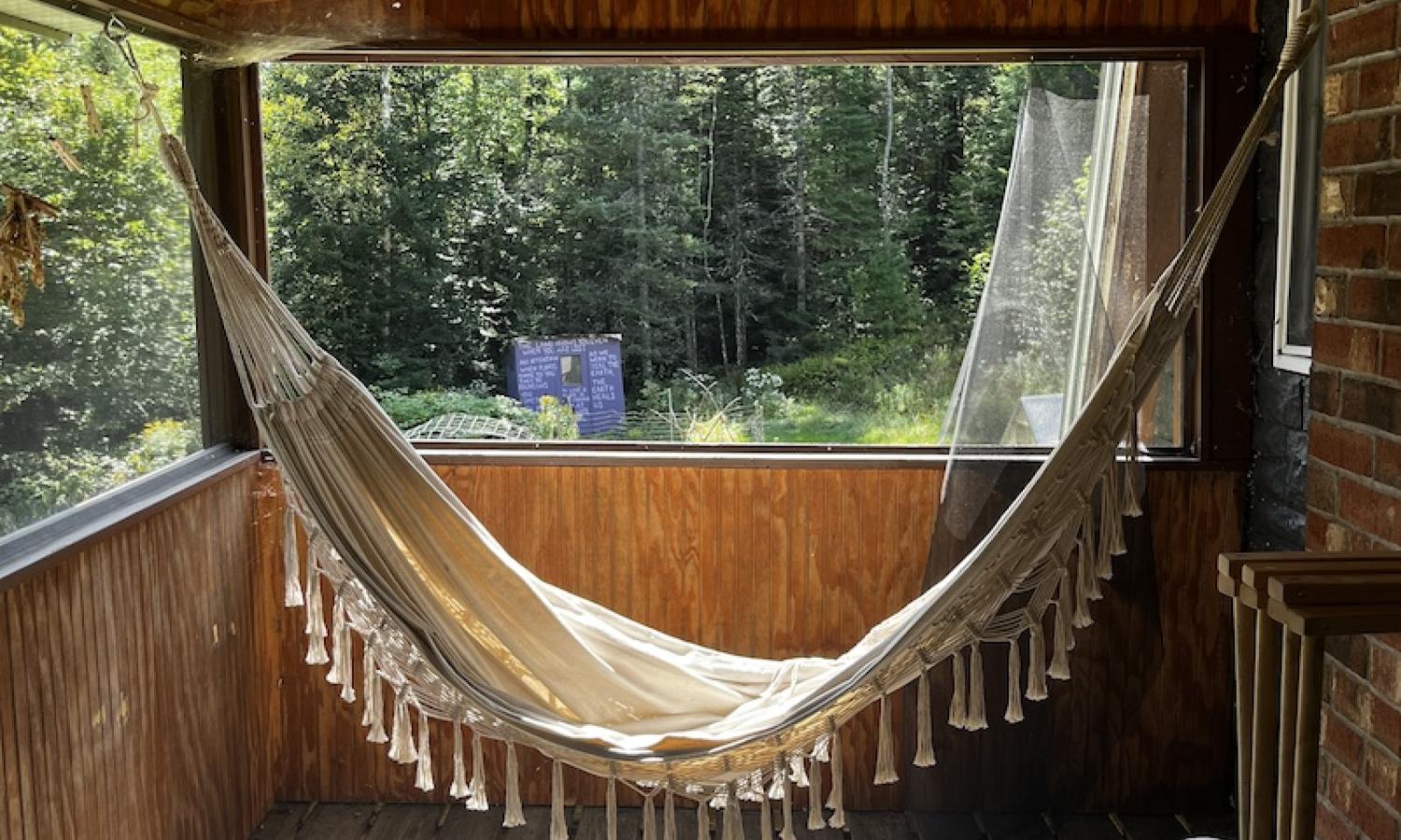 A creme, cloth hammock with tassles hangs on a covered deck