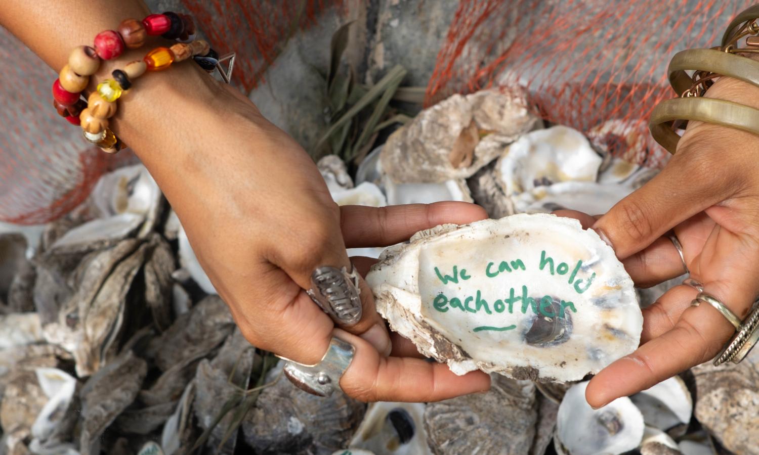 Hands holding an oyster inscribed with "we can hold each other"