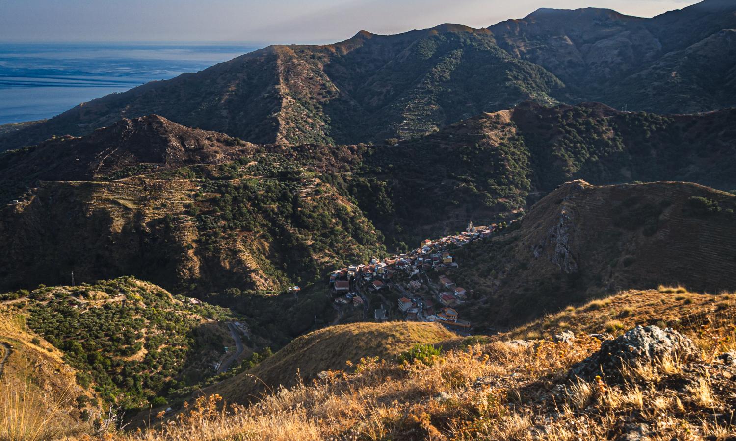 A view of Pezzolo from above showing its location nestled in the mountains, with the Strait of Messina in the background. Photo by Peppe Spuria.